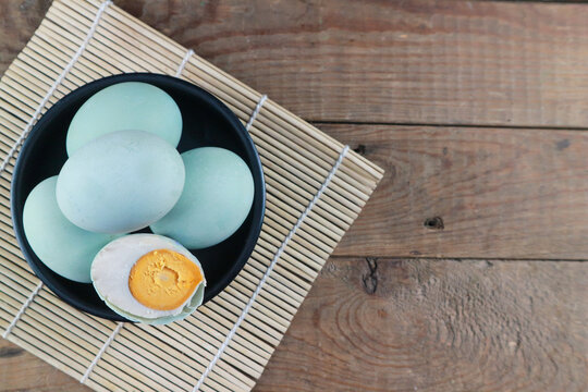 Salted Duck Eggs in Black Bowl on Rustic Wooden Table with Bamboo Mat and Copy Space for Food Design