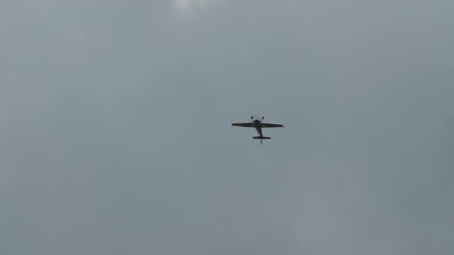 Stunt plane rolling through a maneuver, aerobatic aircraft tumbling against a grey overcast sky, single engine sport plane seen in silhouette at an air show, captured in slow motion