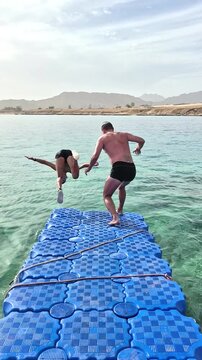 A teenage boy and his father are having fun jumping into the sea from a swaying blue pontoon&mdash;performing somersaults into the Red Sea in Sharm El Sheikh.