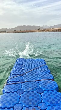 A teenage boy performs a running somersault off a swaying blue pontoon into the Red Sea in Sharm El Sheikh.