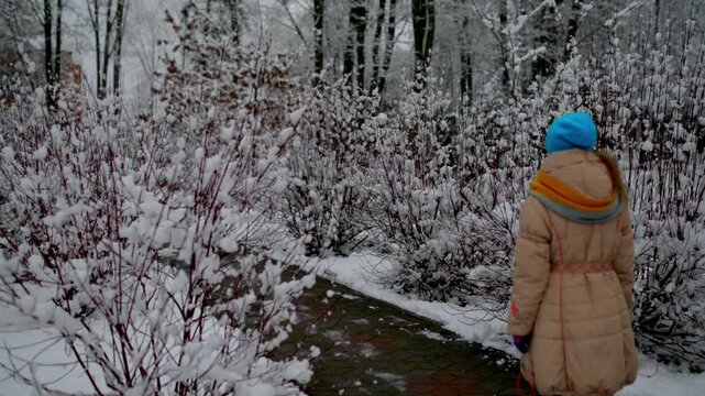 little beautiful girl in a winter jacket walking through a snowy city park