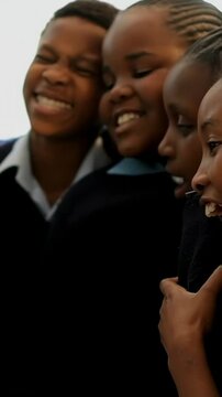 Vertical video: Leaning uniformed students with braids laughing after camera moving in classroom