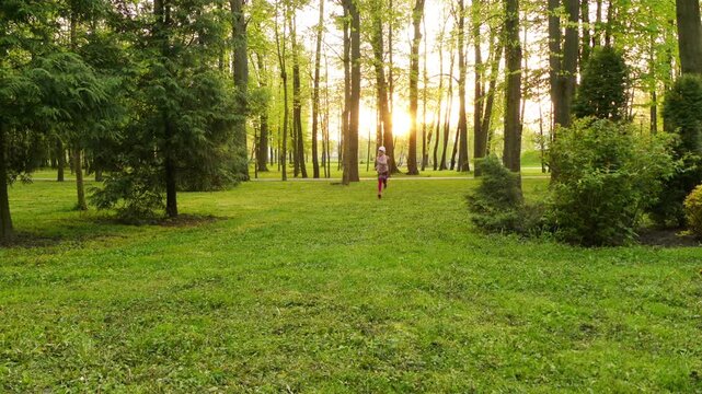 Little beautiful girl runs through grass in summer city park