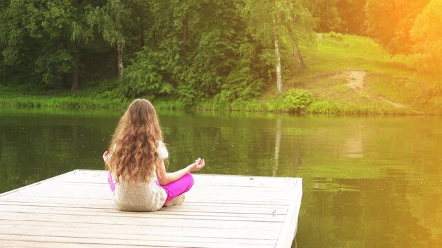 little girl is engaged in yoga on wooden bridge
