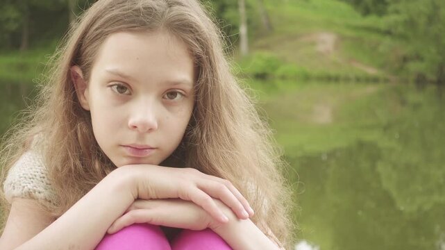 little sad girl is sitting on bridge near lake