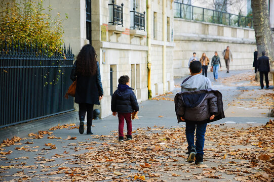 Mother and two sons walking through autumn leaves on a Parisian street, back view of a quiet urban family moment in Paris, France
