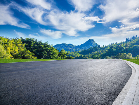 Empty asphalt road and green mountains under clear blue sky