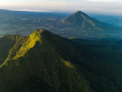Aerial view of Gunung Telomoyo Via Dalangan with lush green mountain slopes and dense forest under golden hour light in Ngablak, Central Java, Indonesia.