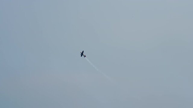 Aerobatic plane climbing away at an angle, single engine stunt aircraft trailing white smoke across a blue grey sky, sport plane at an air show, filmed in slow motion