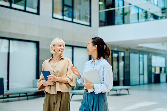Two diverse businesswomen walking and talking in a contemporary office building, representing corporate communication and teamwork