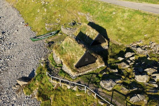 Aerial view of the historic Osvor Maritime Museum with traditional turf-roofed houses and a wooden boat on the rocky shoreline in Bolungarvik, Bolungarvikurkaupstadur, Iceland.