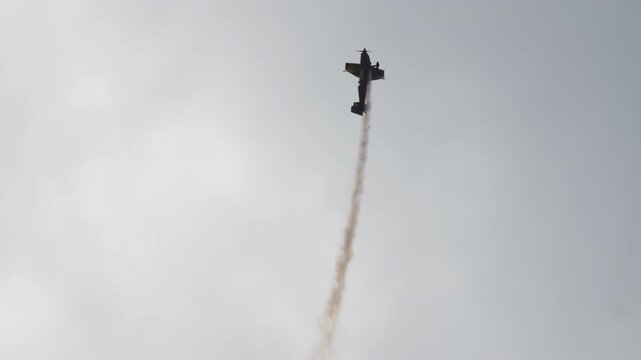 Aerobatic plane climbing straight up, single engine stunt aircraft pulling into a vertical climb with a white smoke trail below, sport plane performing at an air show, filmed in slow motion