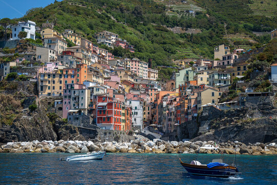 View from the sea of ​​Riomaggiore, one of the  Cinque Terre villages, a steep cascade of pastel houses descending towards a small harbor carved between dark cliffs. Liguria, La Spezia, Italy.