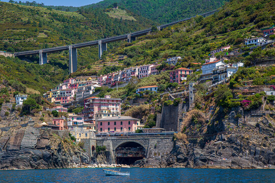 View from the sea of ​​Riomaggiore, one of the  Cinque Terre villages, a steep cascade of pastel houses descending towards a small harbor carved between dark cliffs. Liguria, La Spezia, Italy.