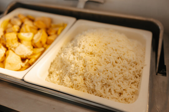 Buffet food display shows fluffy rice beside roasted potato pieces in stainless steel serving trays today