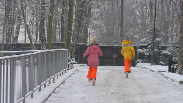 Two little girls in winter costumes run alonga snow-covered road