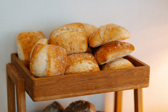 Golden bread rolls rest in wooden tray, showing crisp crusts, warm tones, and cozy baking mood near view