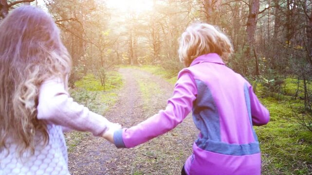 Two little girls run through a pine forest. Slow motion.