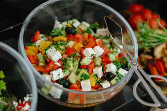 Fresh chopped vegetables with feta, olives, cucumber, peppers and parsley in glass serving bowls nearby