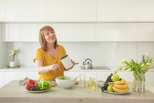 Attractive woman with olive oil in glass jar and organic vegetable on table in kitchen at home. Healthy food concept