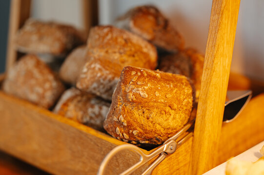 Golden bread loaves rest inside wooden basket, showing crisp crusts, grainy texture and warm bakery light