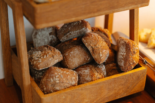 Assorted crusty bread rolls fill wooden basket, lit by warm sunlight, forming bakery market display today