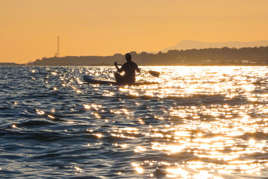 young women  riding  on sup surfing in the sea at sunset