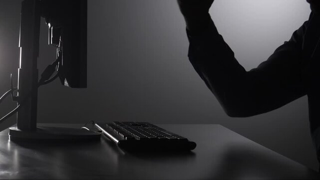 Person's silhouette clenching a fist over a computer keyboard, symbolizing frustration, cyber attack, data breach, and the dark side of internet security