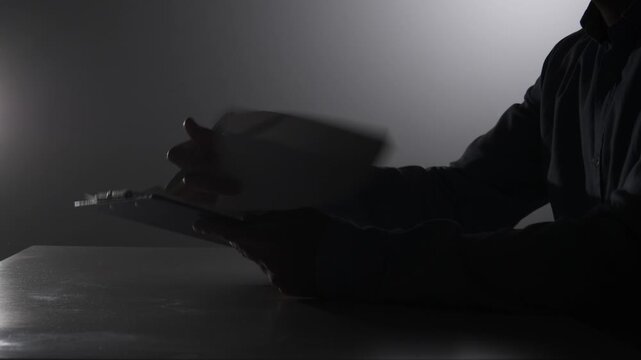 Person's silhouette writing with a pen on a sheet of paper, highlighting concepts of work, legal matters, and business in a dark, focused setting