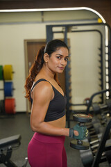 Fototapeta premium Maharashtra, Sion, India- 22nd March 2026- Young Indian girl in her active wear doing workout with dumbbells in gym. 