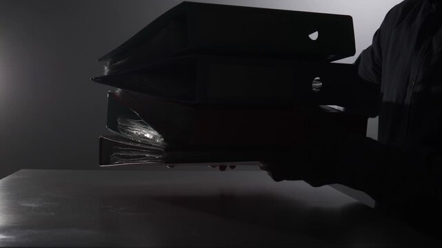 Person handles a towering stack of binders filled with documents, symbolizing the heavy workload, bureaucracy, and overwhelming administrative tasks in an office environment
