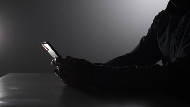 Silhouette of a person holding a modern smartphone in dark surroundings, representing concepts of internet security, digital privacy, hacking, data theft, and online vulnerability