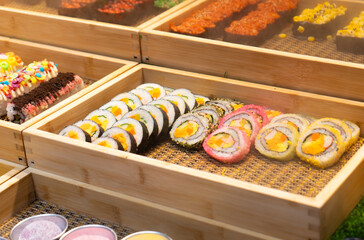 Assorted maki sushi and kimbap rolls in traditional style, vibrant yellow and pink colors, representing a fresh Asian buffet presentation used for restaurant display © Arnepi