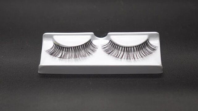 A black false eyelashes on a white tray against black background.
