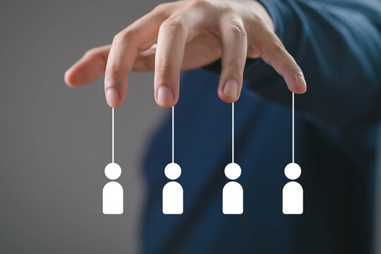 Hand controlling human icons like puppets, representing leadership control, team management, influence, authority, workforce manipulation, organizational power, and strategic decision making.
