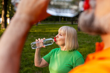 Naklejka premium Senior woman drinking water staying hydrated in a park