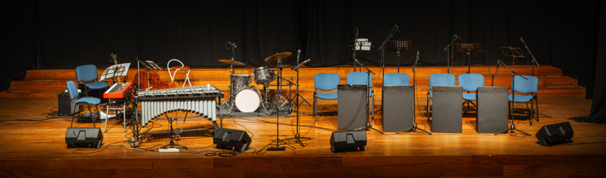 Wide panoramic view of an empty concert stage prepared with drum kit, metallophone, microphones, chairs, music stands and floor monitors before musicians arrive