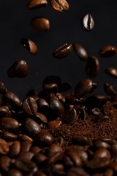 Roasted Coffee Beans Falling onto Fresh Ground Coffee on Dark Background
