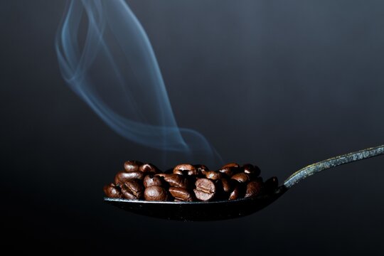 Aromatic Coffee Beans on Spoon with Swirling Smoke Trail on Dark Backdrop