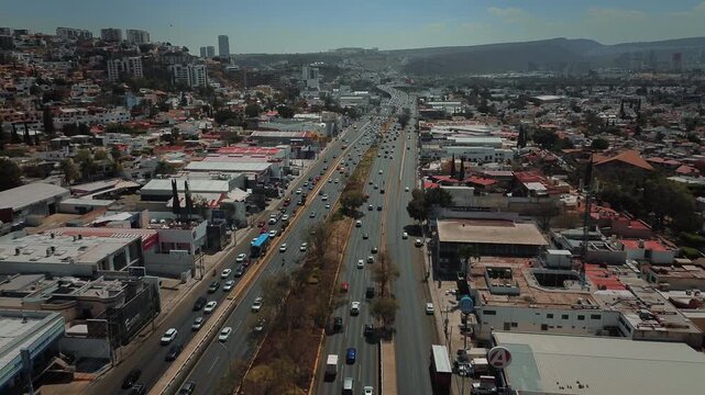 Expansive aerial view advancing along Boulevard Bernardo Quintana with moderate traffic flow extending toward distant horizon surrounded by urban development and mountain exposition center backdrop