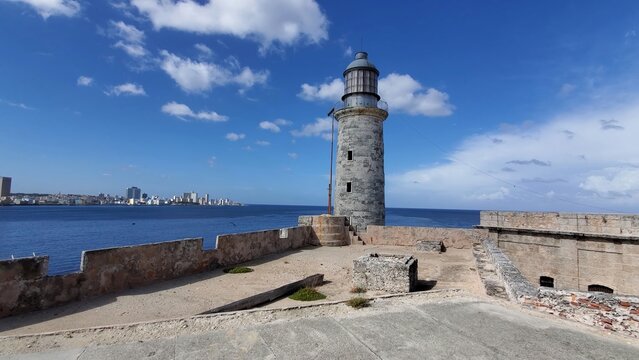 View of the historic El Morro lighthouse on the stone ramparts of the fortress overlooking the Caribbean Sea and Havana skyline under a blue sky in Havana, Havana, Cuba.
