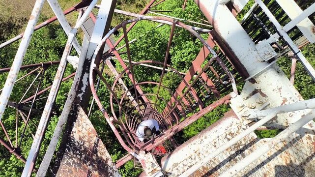 Man climbing vertical cage ladder inside 75m repurposed radar tower