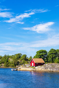Rote Holzh&uuml;tte und B&auml;ume an der K&uuml;ste der Insel Ross&ouml; nahe Str&ouml;mstad, Schweden