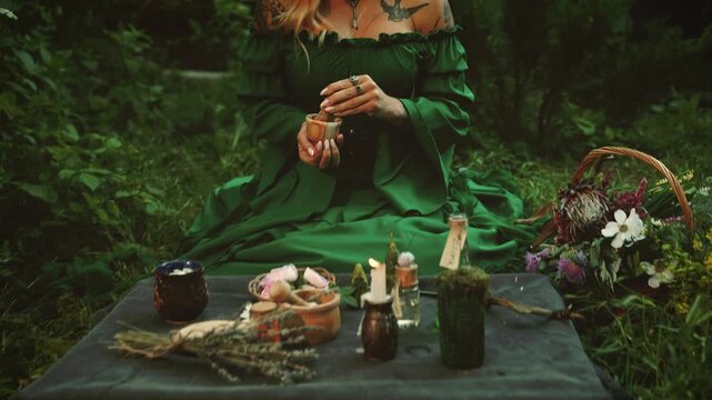 silhouette woman sitting at table on green grass summer garden, boho gothic detail glass, candles forest. elf mystical girl holds stone mortar in hands creating powder healing potion, grinds spices 