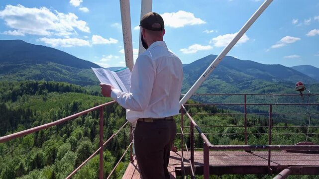Man in white shirt reading documents and inspecting metal structure on 75m tower platform