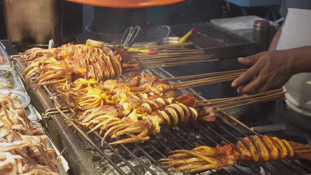 Street vendor is grilling squid satay at a food market