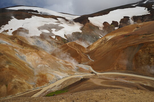 View of the geothermal landscape of Kerlingarfjoll with steaming vents, colorful rhyolite mountains, snow patches, and a winding river in Hella, Rangarthing ytra, Iceland.