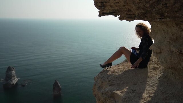 Woman cliff sea, dramatic view of beautiful girl sitting on rocky ledge above the dark ocean waves.