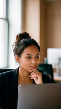 Pensive young businesswoman thinking while working on laptop in contemporary office space