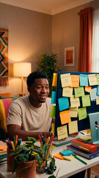 Young man working at home desk surrounded by colorful sticky note reminders